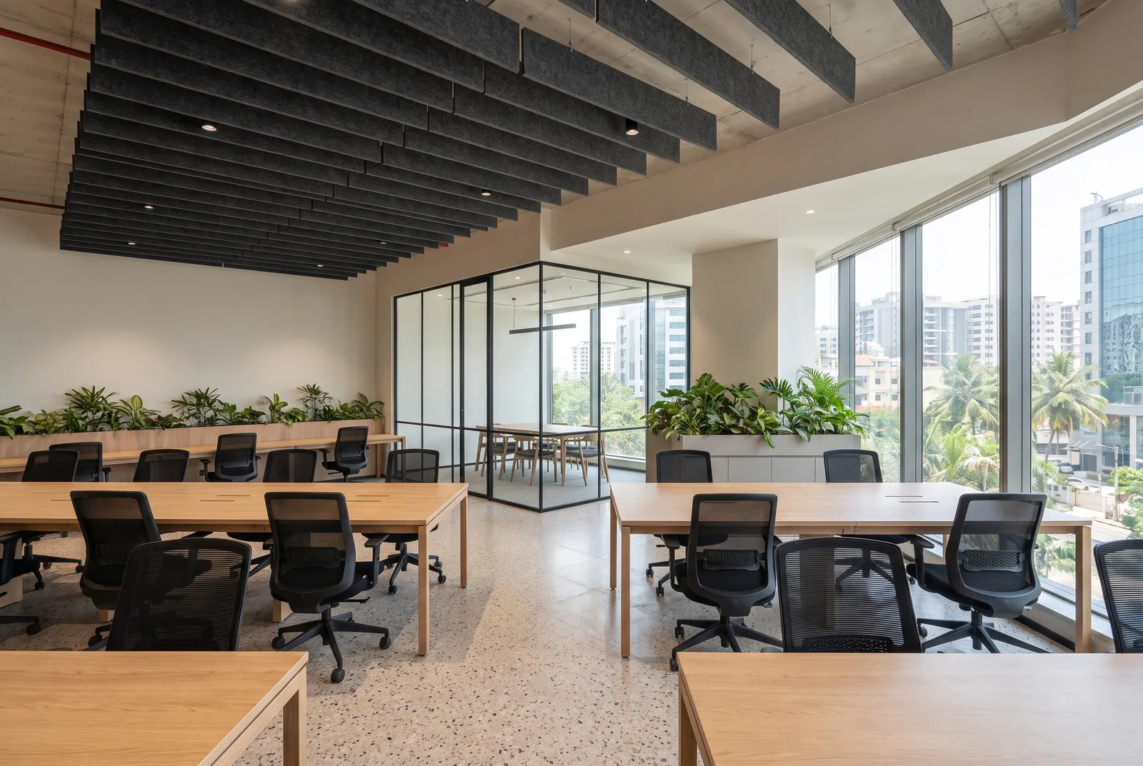 Open-plan office interior with acoustic ceiling baffles and a glass-partitioned meeting room